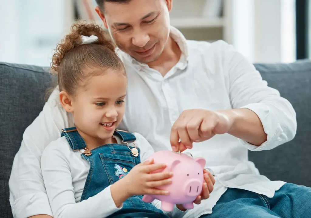 happy-girl-saving-money-with-dad-indoors-2026-03-25-02-50-15-utc